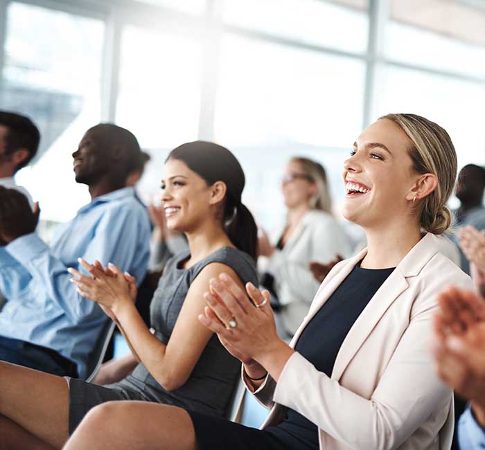 a group of business people applauding while sitting in a lecture room during a seminar